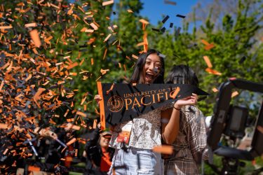 student surrounded by orange and black confetti holding a pacific pendant 