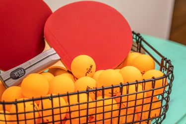 Ping pong paddles in a basket of orange balls.