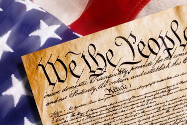 The first page of the US constitution on top of the American flag.