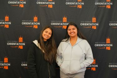 two students posing in front of orientation background