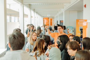a group of students is gathered around in a large space talking with one another
