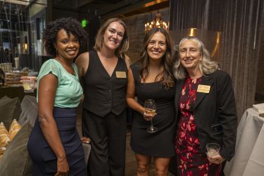 Four individuals dressed in business attire in an indoor setting smiling at the camera