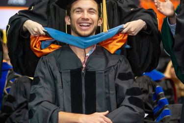 Student getting hooded on stage during TJL School of Pharmacy Ceremony