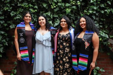 Four students posing for a picture with graduation sash.