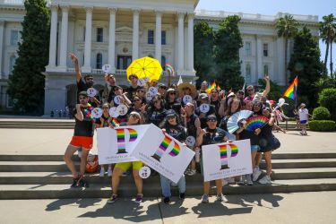 A group of people in black t-shirts smile and pose with rainbow flags