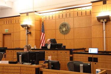 An image of a court room with a just sitting in the center with a clerk sitting in front of them. 