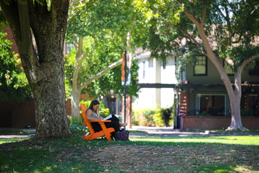 A women sits in a orange chair reading a book. 