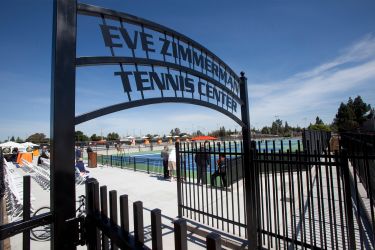 a metal sign reads "Eve Zimmerman Tennis Center" in front of a tennis court