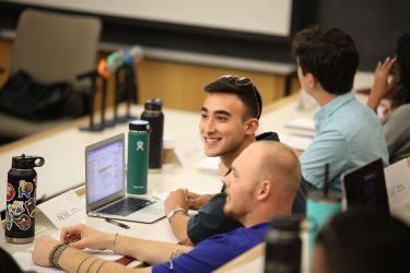 A student smiles while working in class on his laptop. 