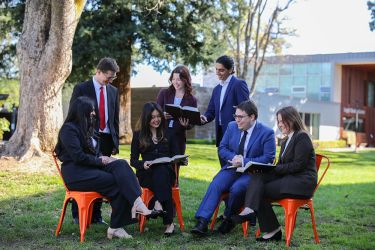 A group of seven students stand outside glancing at law books and laughing. 