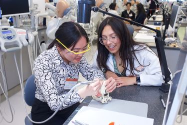 two women at a desk with one of them holding a drill and a typodont