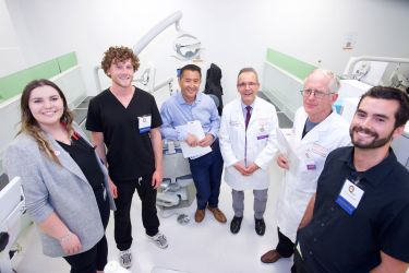 6 people standing in a semi circle facing the camera in the sim lab