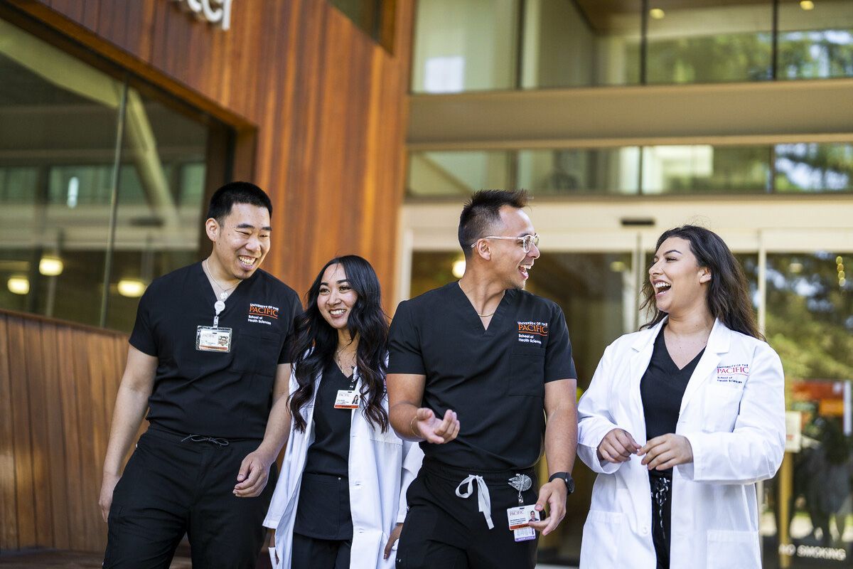 Photo shows four Nursing students at Pacific's School of Health Sciences talking and smiling while walking out of the nursing classroom.