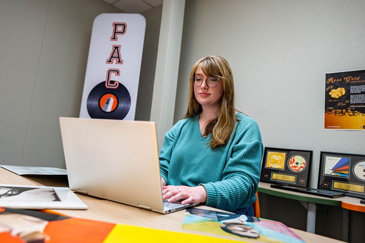 college student sitting at a desk with a laptop and vinyl albums