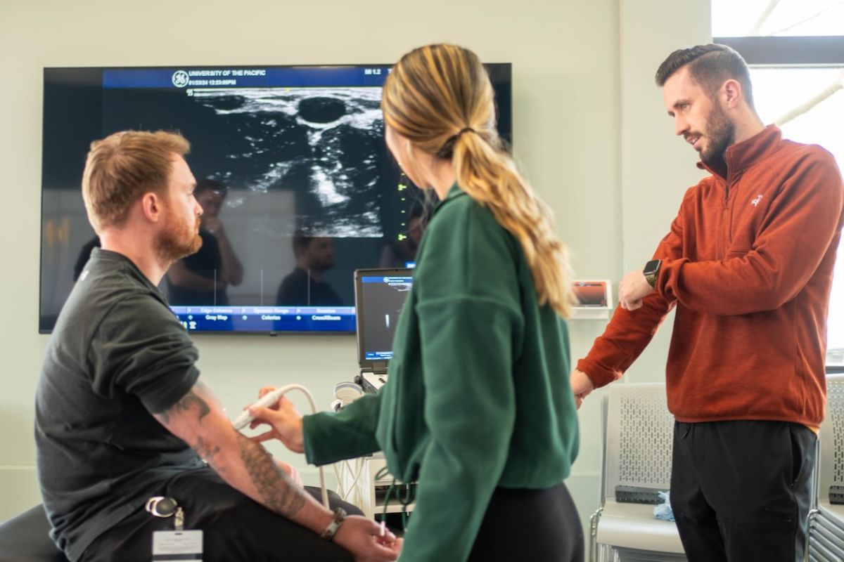 Photo shows three PA students practicing using diagnostic equipment.