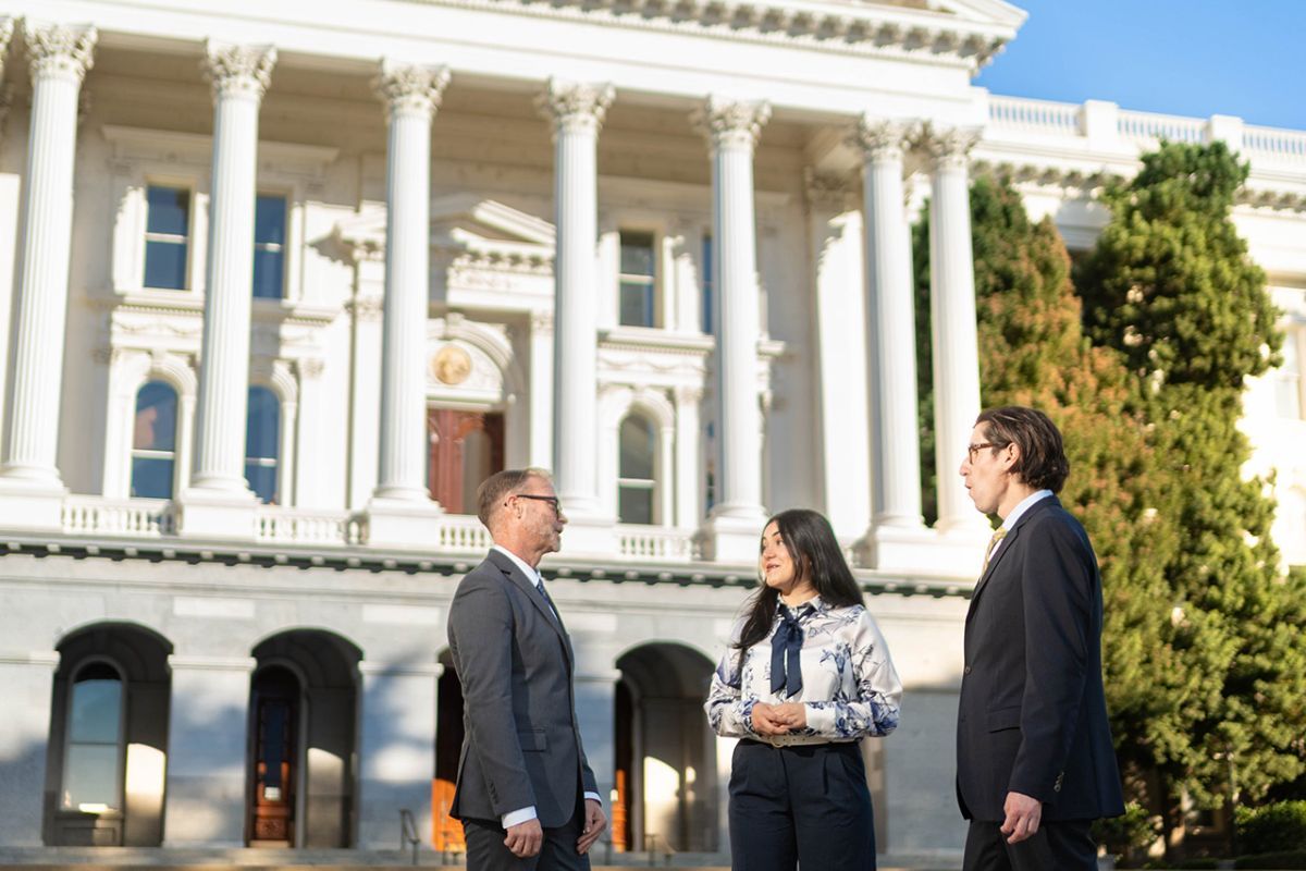 three individuals standing in front of the Sacramento Capital Building. 
