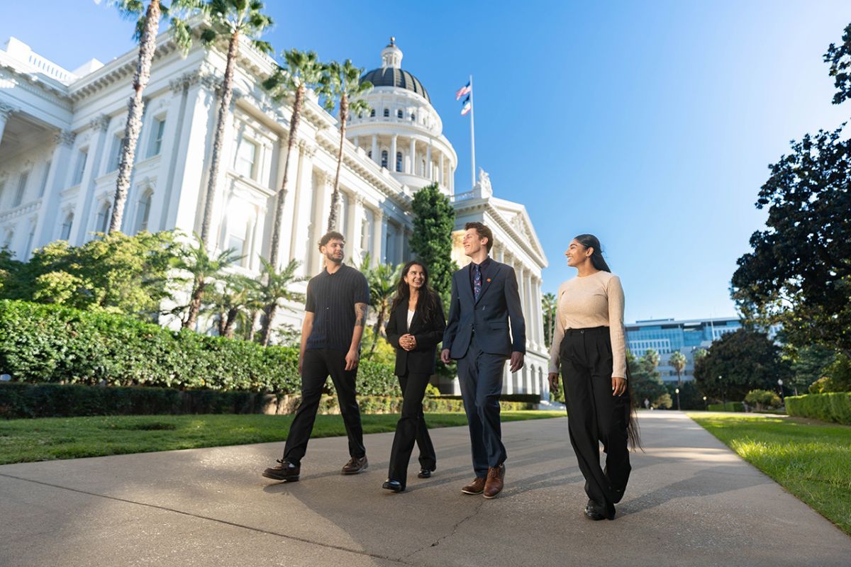 Image of 4 individuals walking in front of the Sacramento Capital Building. 