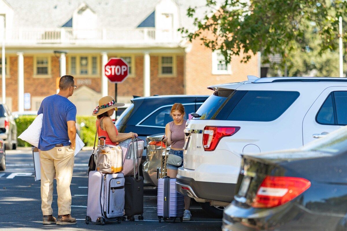 students unload a car in front of a greek house