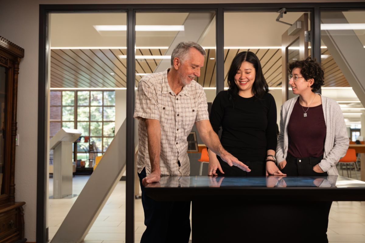 three people stand together looking at a table