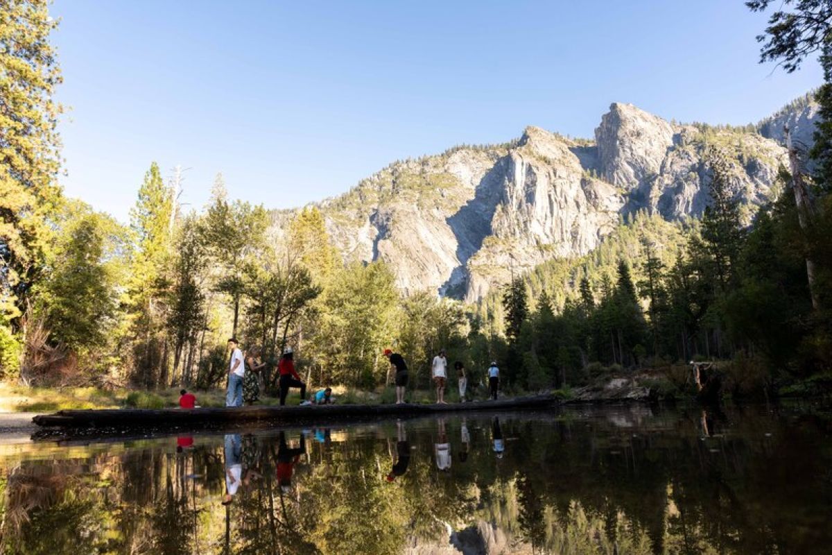 students stand under a mountain and next to a body of water
