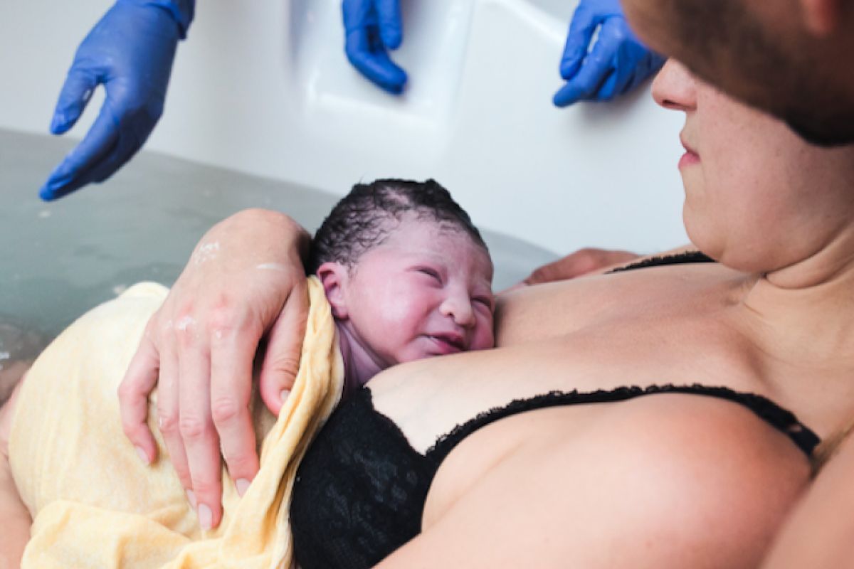 A newborn infant is shown being held by the mother in a birthing tank.