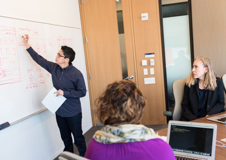 person writing on whiteboard in front of co-workers