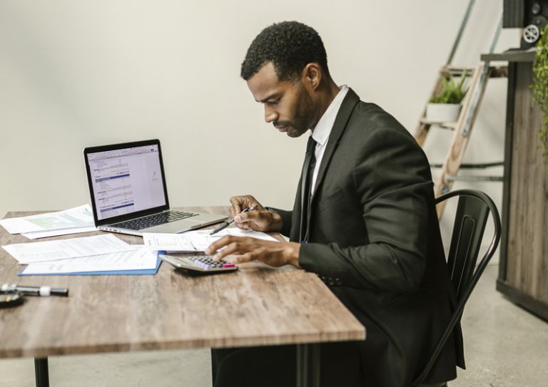 Man sitting at table with calculator and laptop