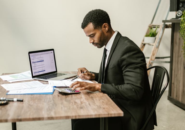 Man sitting at table with calculator and laptop
