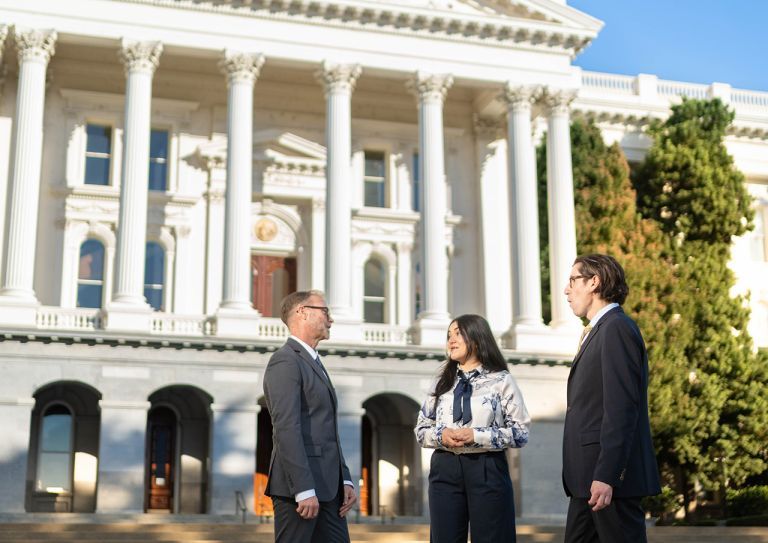 three individuals standing in front of the Sacramento Capital Building. 