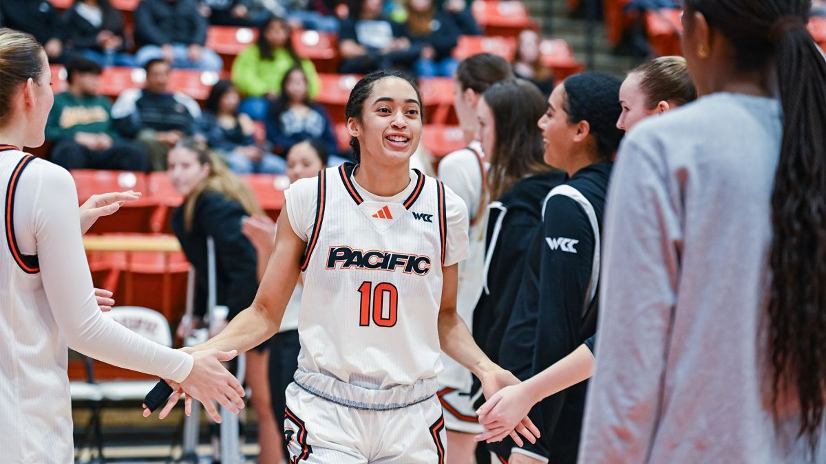 A Pacific women's basketball player high fives other players on the basketball court.