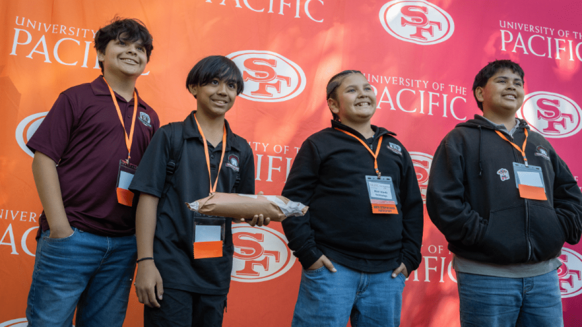 Students smiling in front of 49ers and Pacific branded backdrop