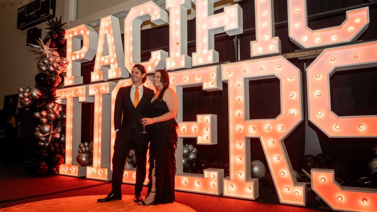 Two people dressed in black in from of a Pacific Tigers sign