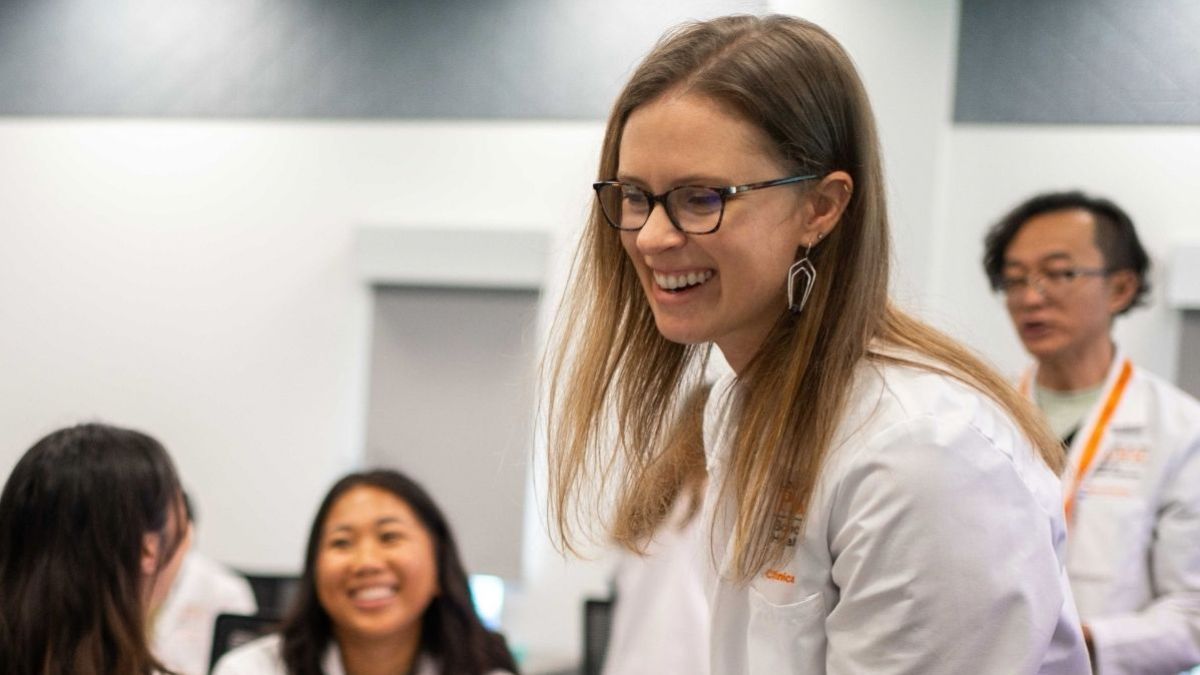 A faculty member in a lab coat smiling in the foreground