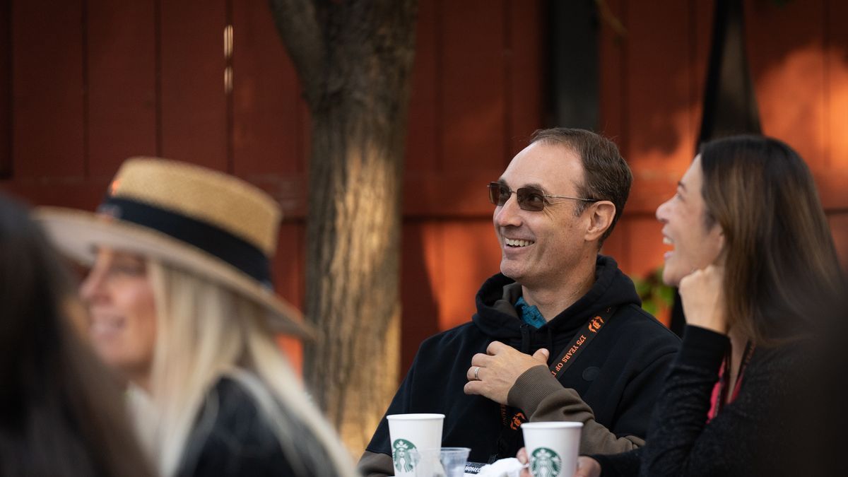 A parent in sunglasses and a black jacket smiles at Homecoming and Family Weekend