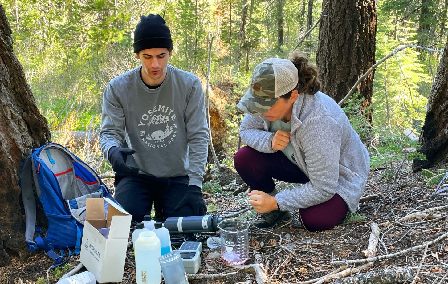 Students sitting in field with materials for collecting water samples.