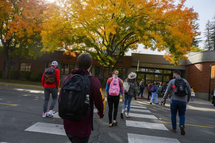 Students wearing backpacks cross the street during a fall day.