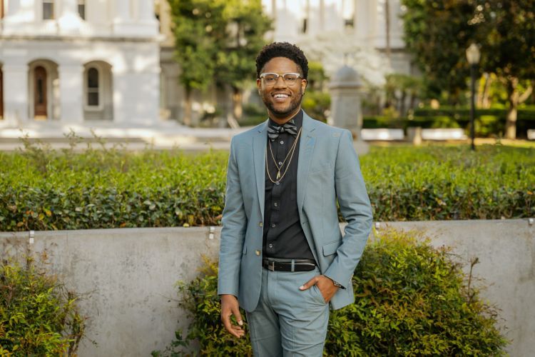 A Black man standing outside the California State Capitol Building, smiling.