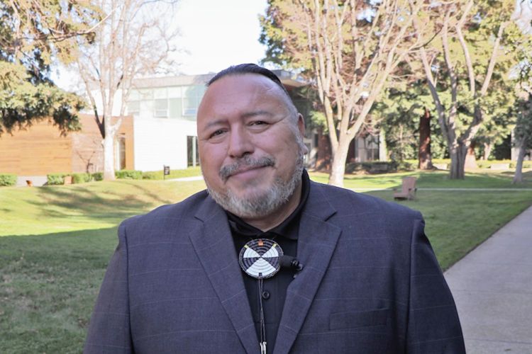 A man in a suit and bolo tie stands outside of the library building