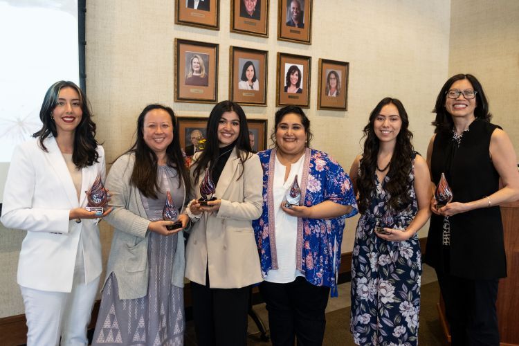 Six women stand together holding awards at ceremony