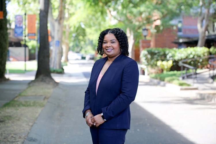 A woman in a navy suit poses outside smiling.