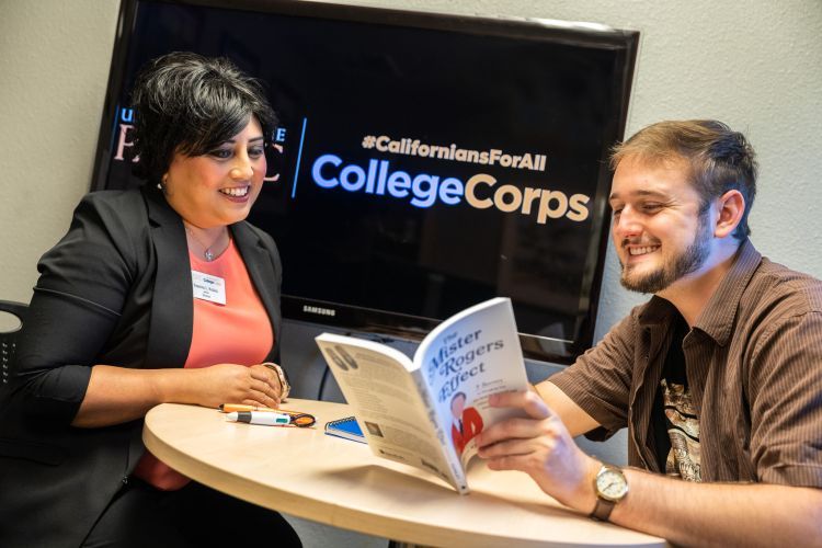 Two people sitting at a desk looking at a book.