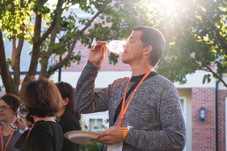A man stands outside sipping from a wine glass