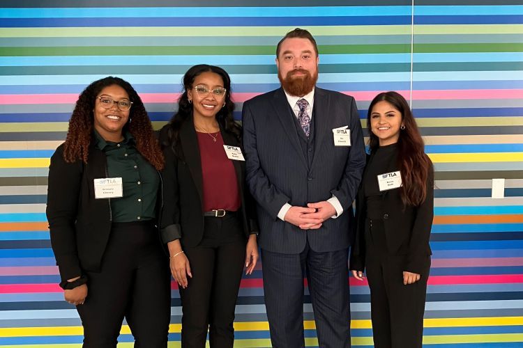 Four students pose for a photo in front of a colorful wall