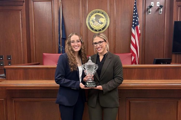 Two female students hold a trophy in a courtroom