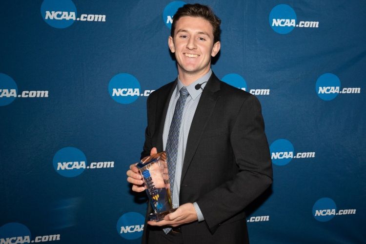 Liam Egan holds an award in front of blue background reading Elite 90