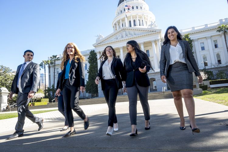 Five people walk and chat with each other in front of the CA Capitol Building