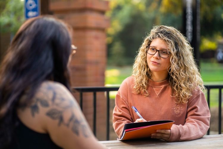 a social work student sits a table holding paperwork while talking to a patient