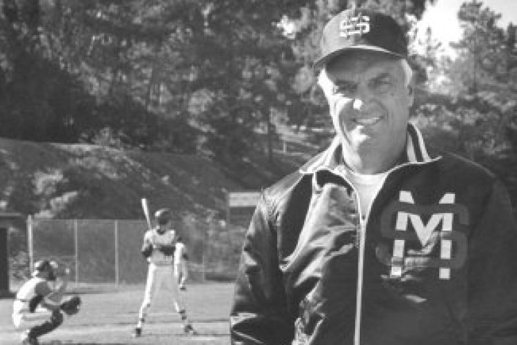 A black and white image of John Noce standing on a baseball field