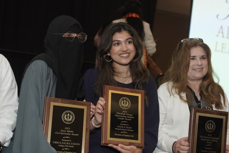 three people stand together holding their award plaques