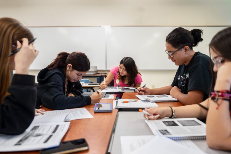 students sit at a table looking at books